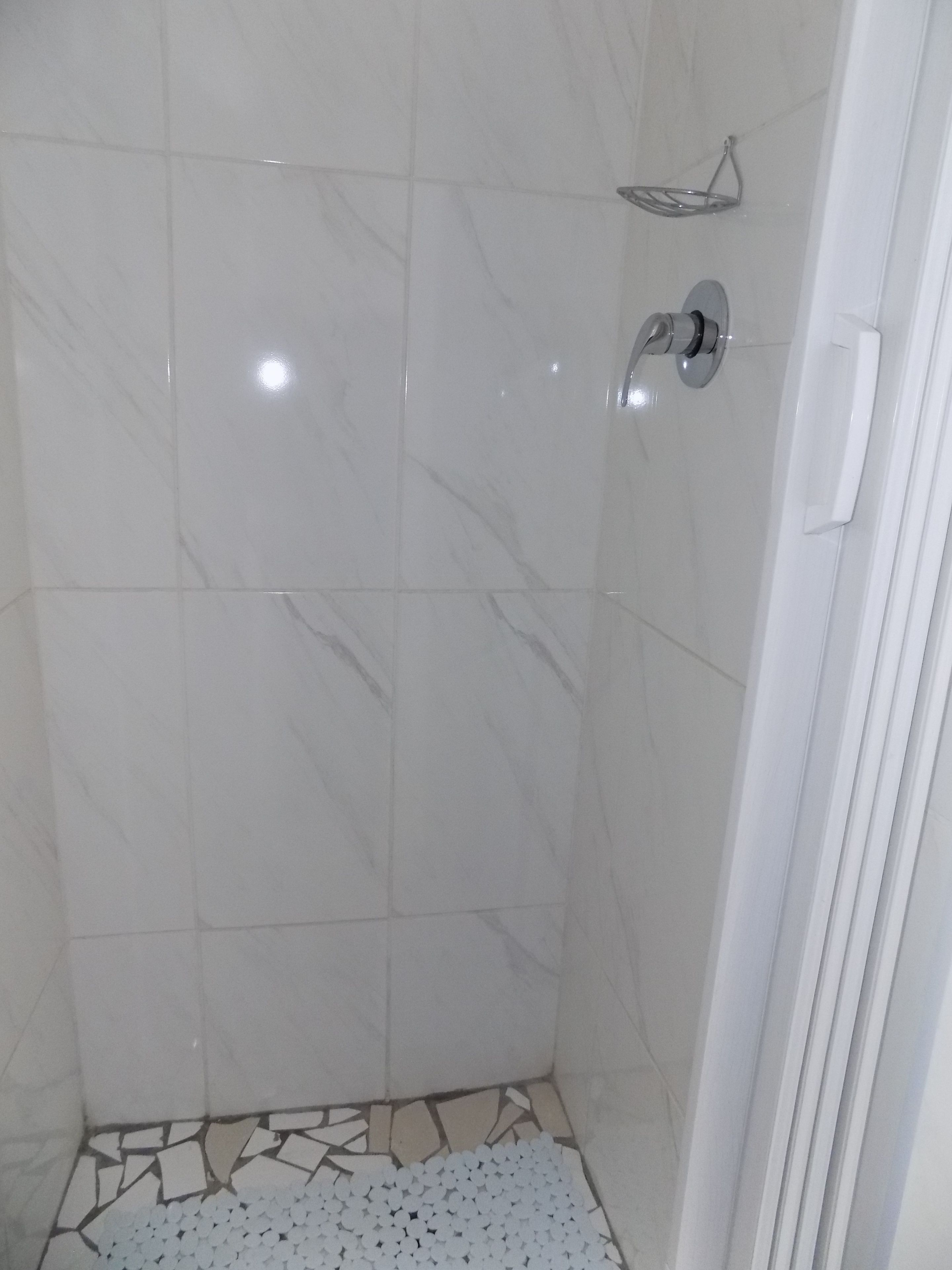 A bathroom with white marble tiles, a shower area, and a tiled floor with a mosaic pattern.