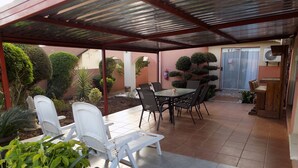 A covered patio area with a table and chairs, surrounded by potted plants and a fire extinguisher. - Joezebel Guest House (Moses Kotane)