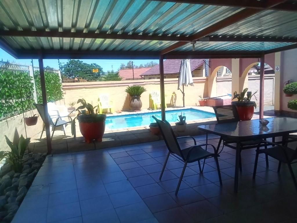 A covered outdoor area with a pool, potted plants, and a table with chairs.