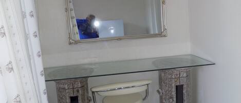Un baño con un lavabo de vidrio, un espejo encima y un cubo de basura al lado del lavabo.