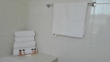 A bathroom with white tiled walls, a white towel rack with a folded towel, and a stack of white towels.