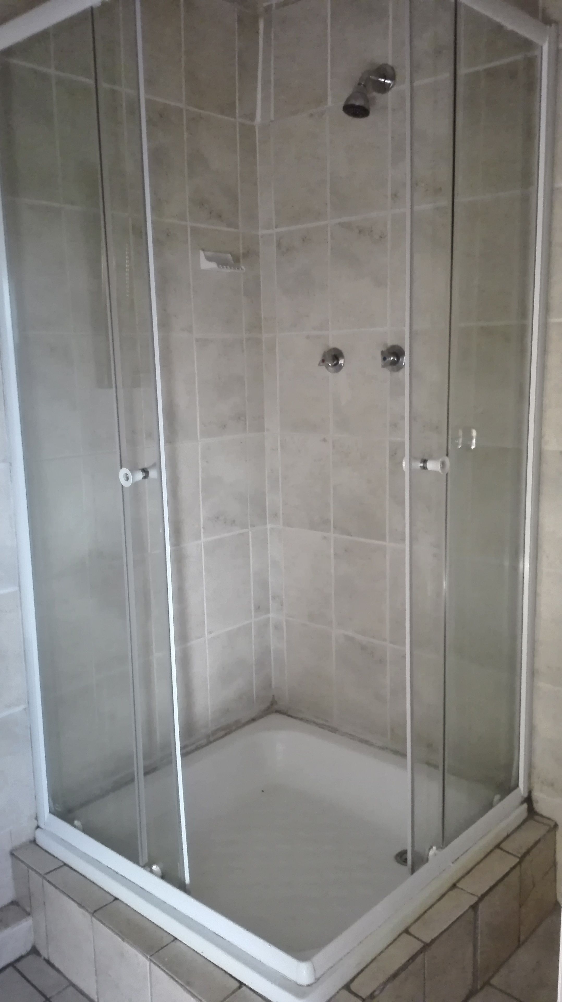 Un espace de douche d’angle avec des portes en verre transparent, un sol carrelé et une pomme de douche.