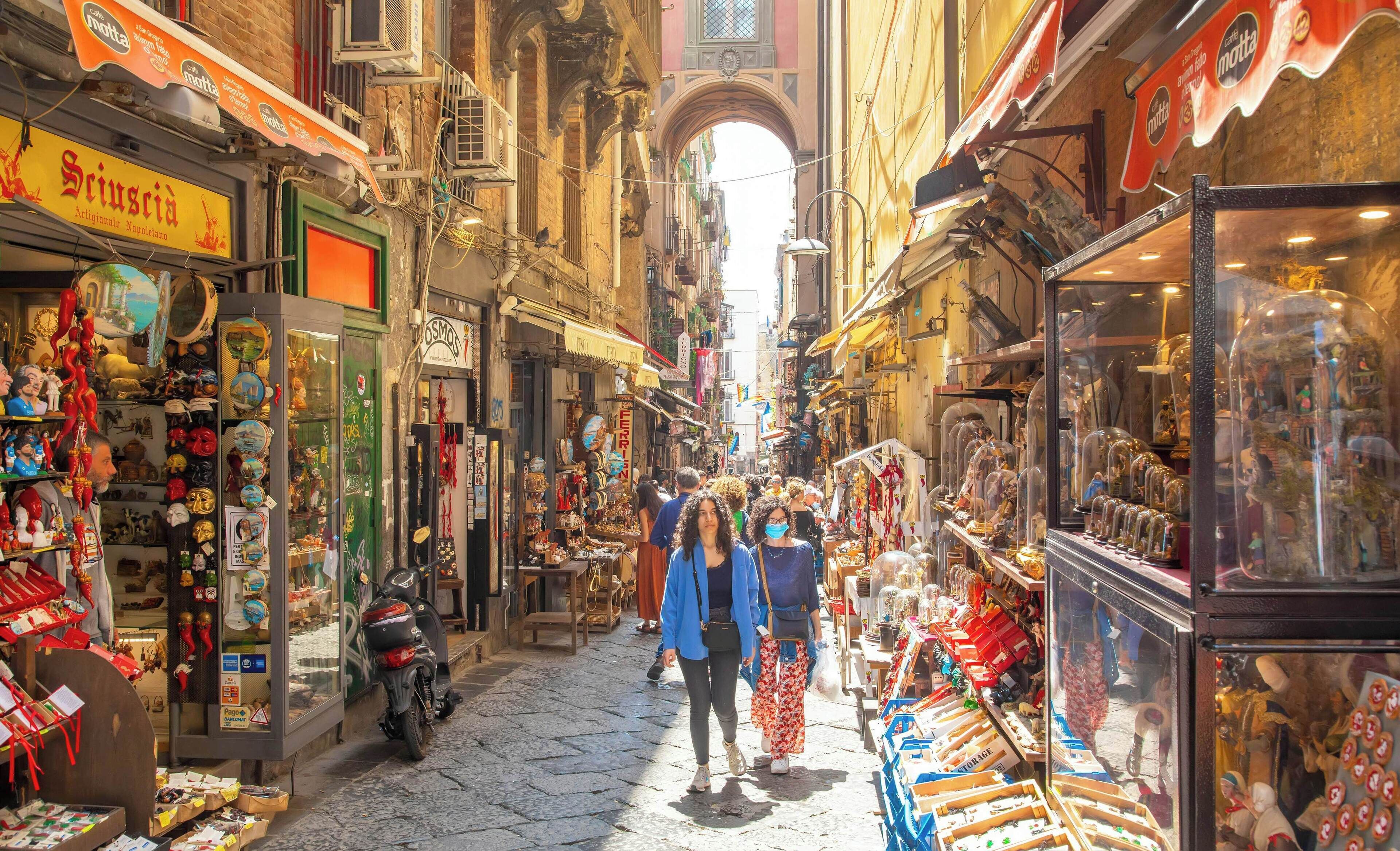 A narrow street with shops on both sides, including a visible sign for 'Scuoccia Artigianato Napoletano'.