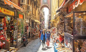A narrow street with shops on both sides, including a visible sign for 'Scuoccia Artigianato Napoletano'.