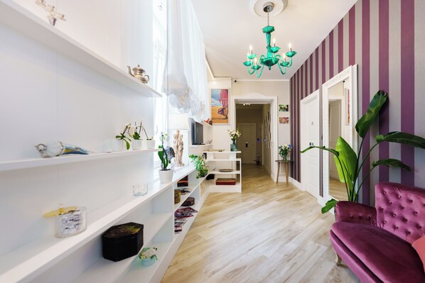 A hallway with white shelves, a purple chair, and a green chandelier.