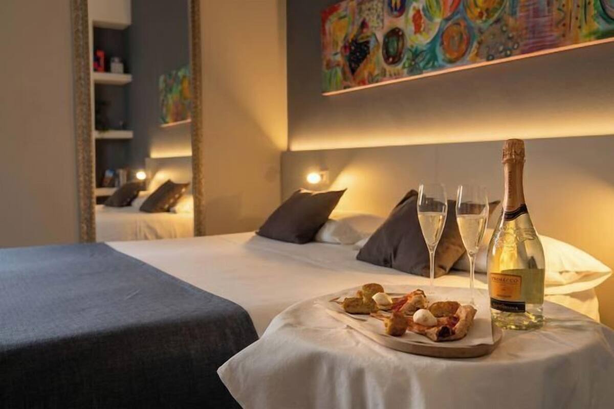 Ein Hotelzimmer mit Bett, einem kleinen Tisch mit Speisen und Getränken sowie einer Flasche Alkohol.