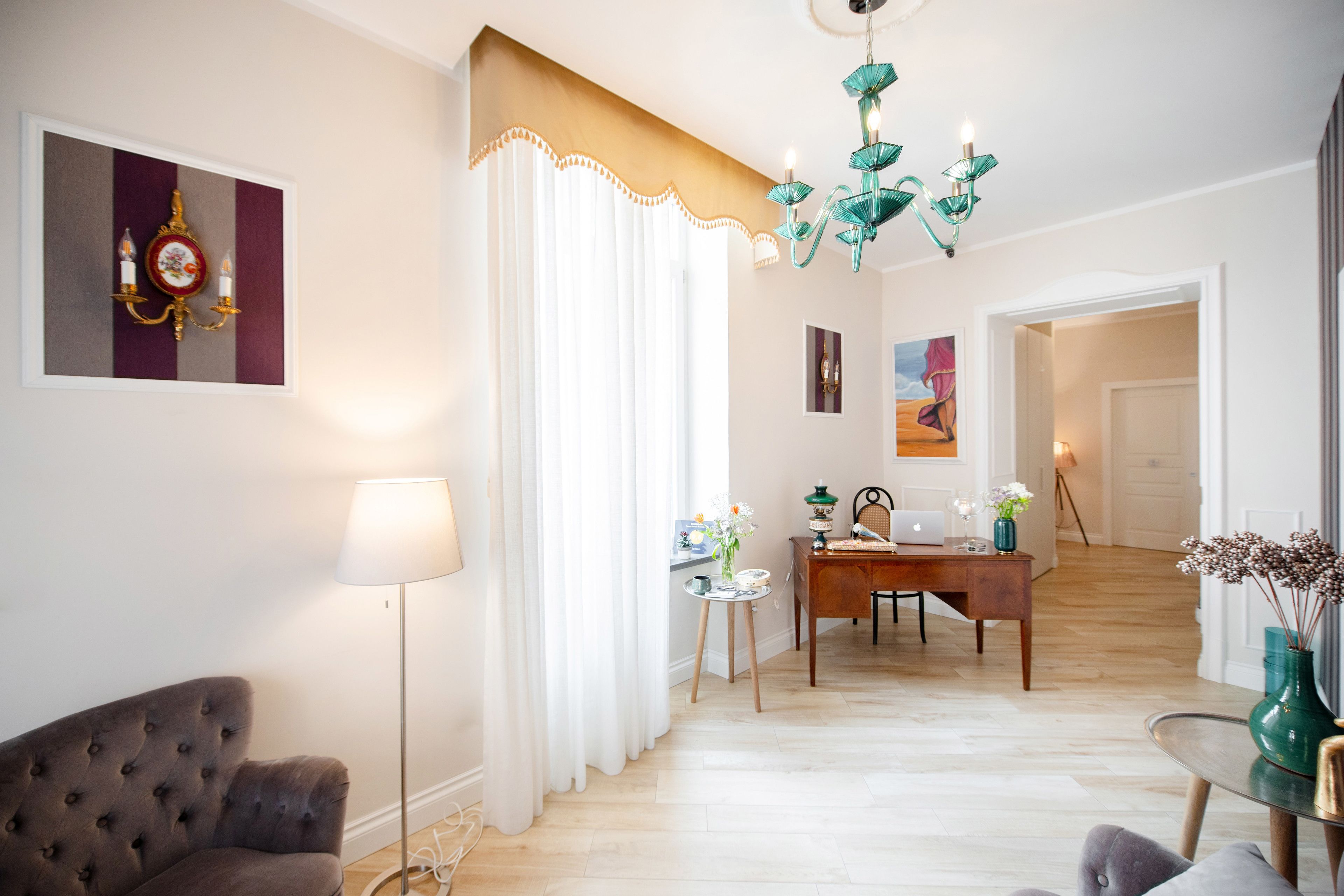 A well-lit living room with a sofa, a lamp, a dining table with chairs, a chandelier, and a painting on the wall.