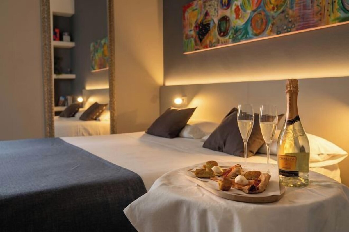 Camera d'albergo con un letto, un tavolino con cibo e bevande, e una bottiglia di alcolici.