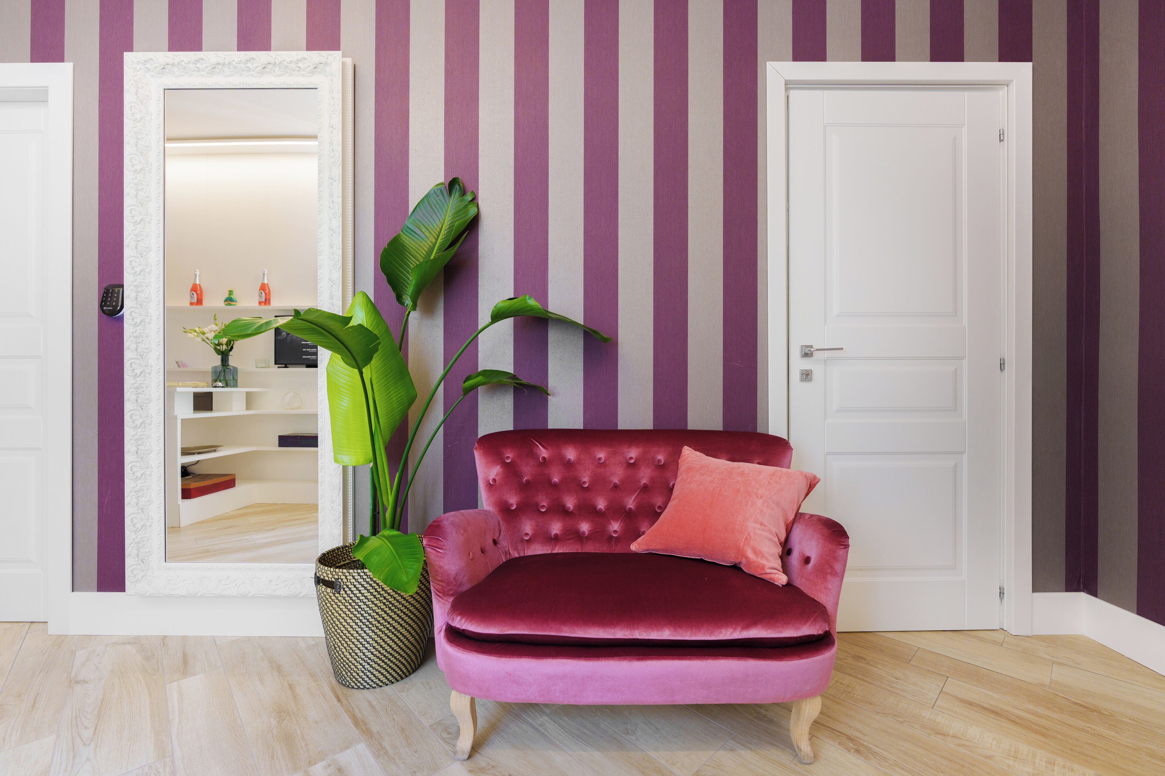 A room with a red velvet sofa, a potted plant, and a striped wall.