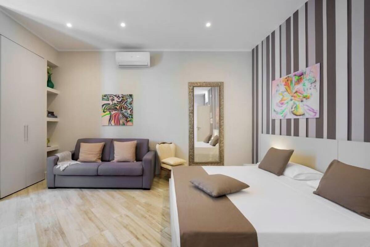 Ein modernes Hotelzimmer mit Bett, einer Sitzecke, einem Spiegel und Bildern an den Wänden.