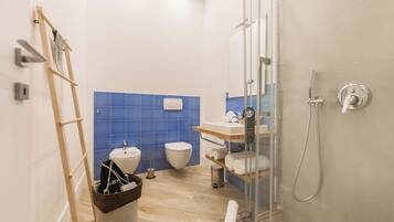 A modern bathroom with a glass shower enclosure, a wooden ladder, a white sink, and a blue-tiled wall.