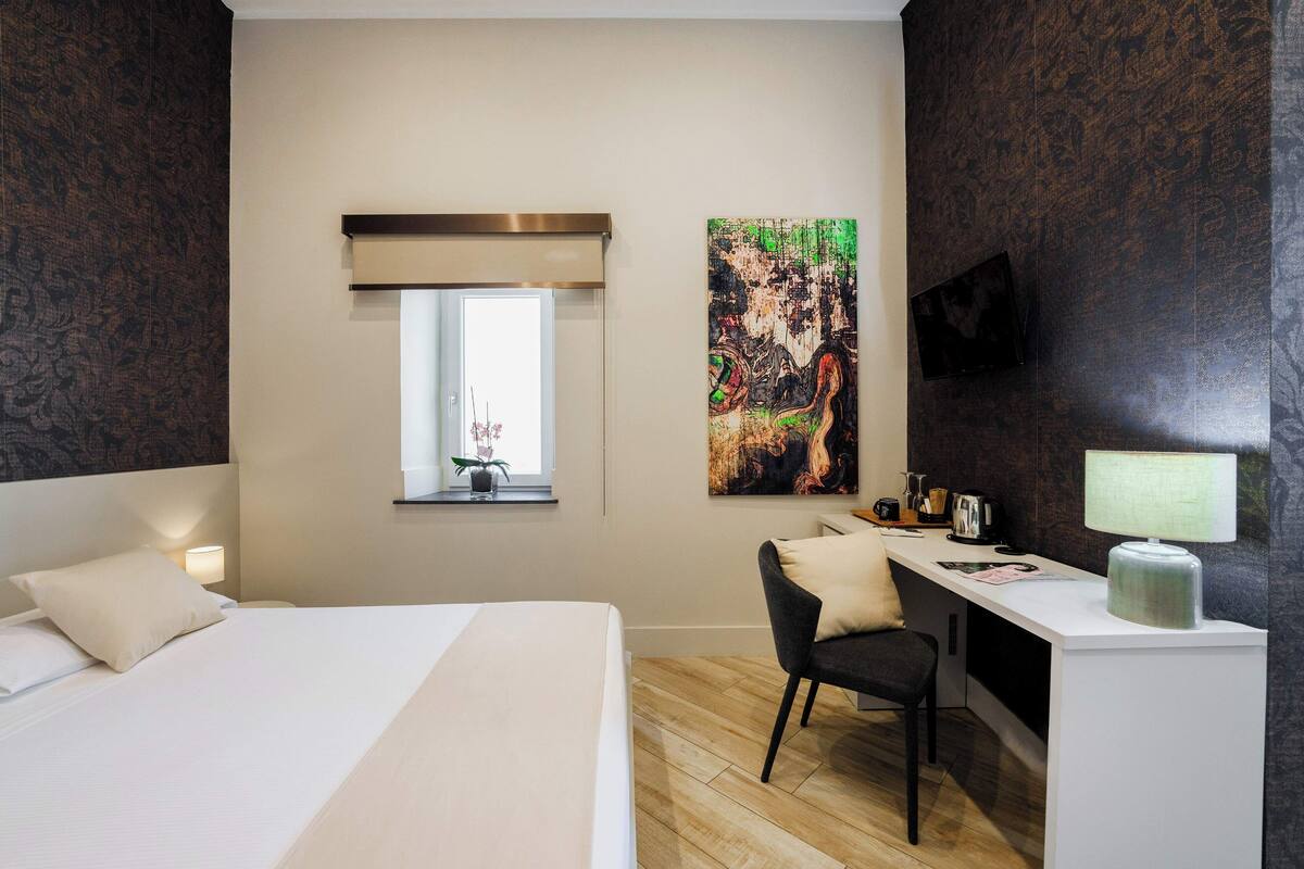 Ein Hotelzimmer mit Bett, Schreibtisch, Stuhl und einem großen, abstrakten Gemälde an der Wand.