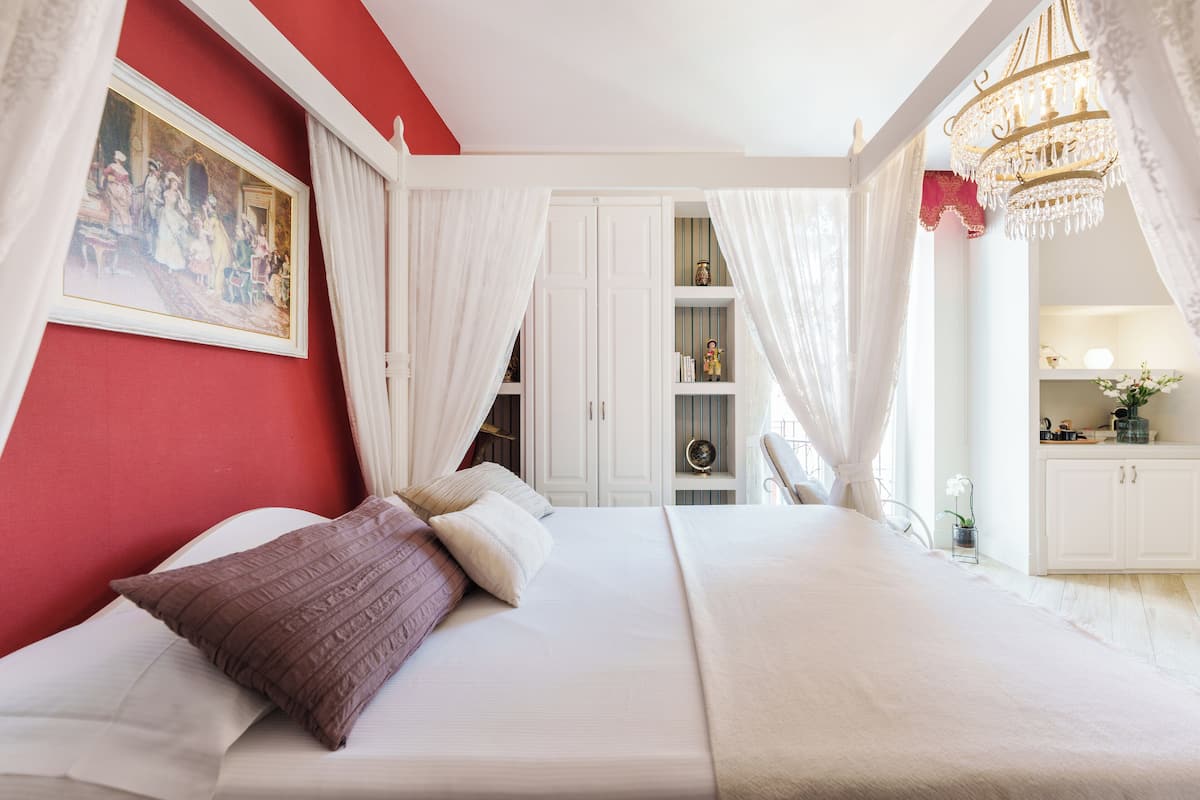 Ein Schlafzimmer mit einem großen Bett, weißen Vorhängen, einer Chandelier und einem Gemälde an der Wand.