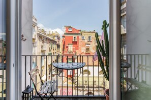 A balcony with a table and chairs, a cactus, and a view of colorful buildings.