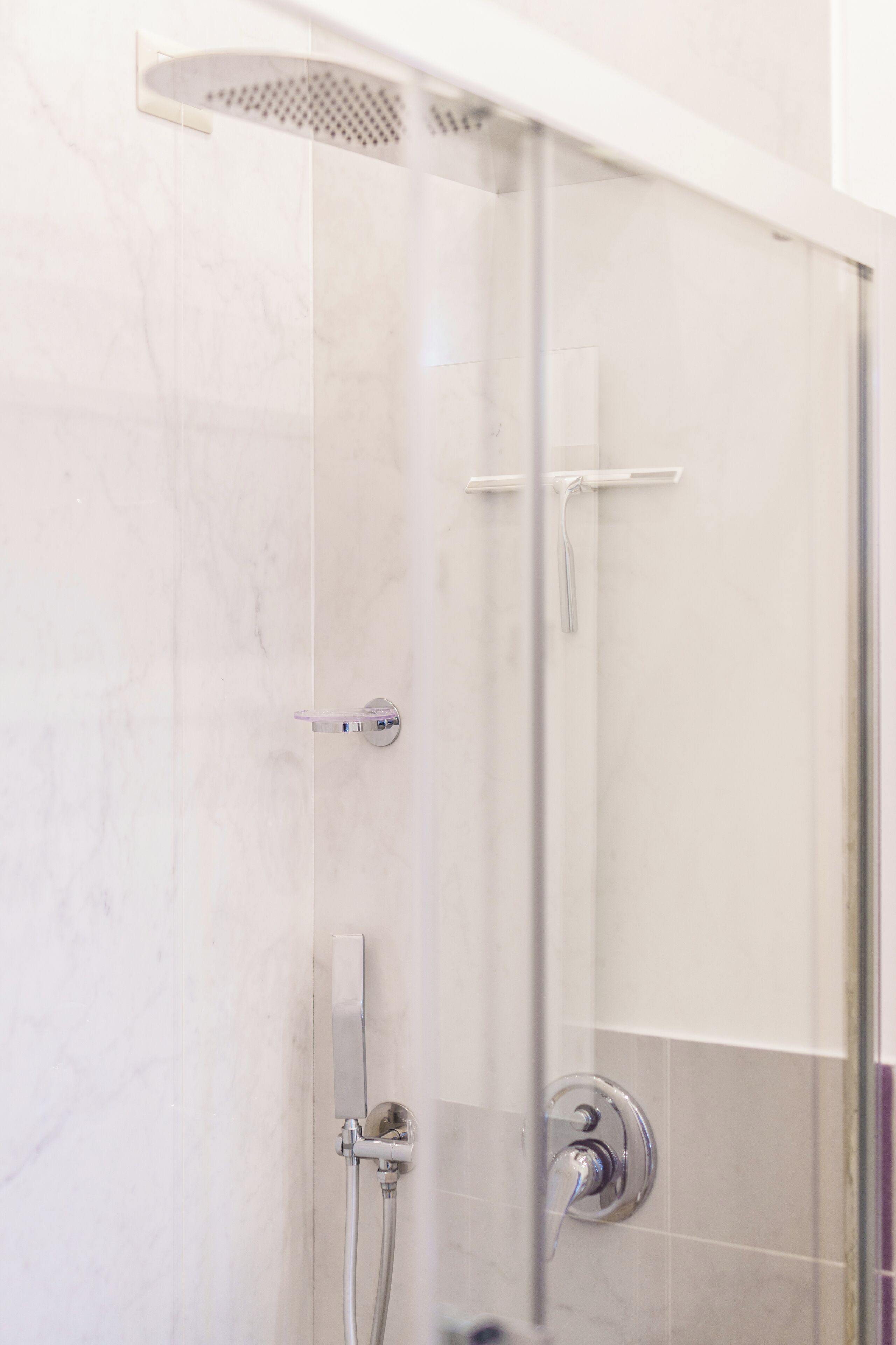 A modern shower enclosure with a glass door, a handheld showerhead, and a wall-mounted control panel.