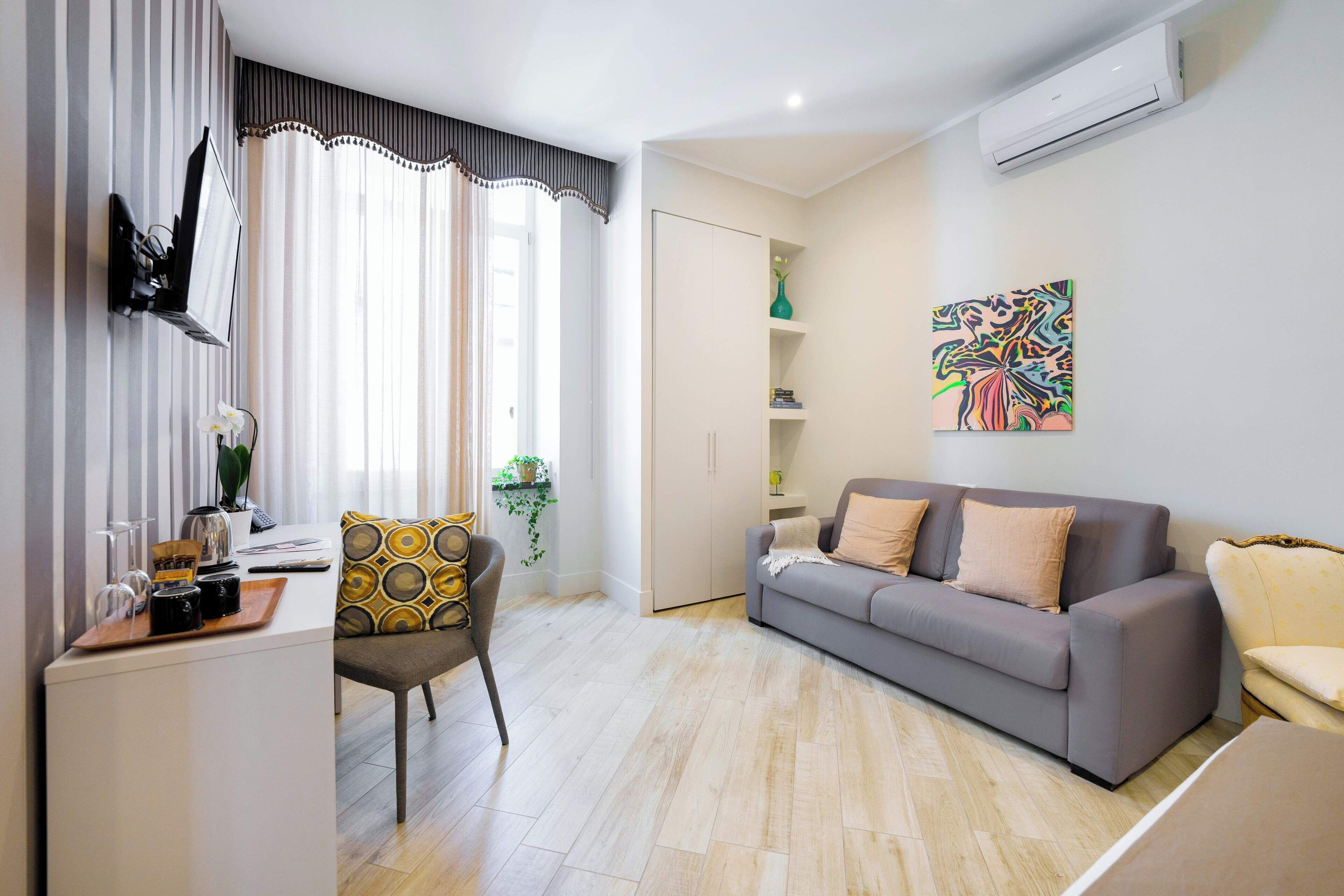 Uma sala de estar moderna com um sofá cinzento, uma mesinha com uma cadeira, uma TV fixada na parede e um quadro abstrato colorido na parede.