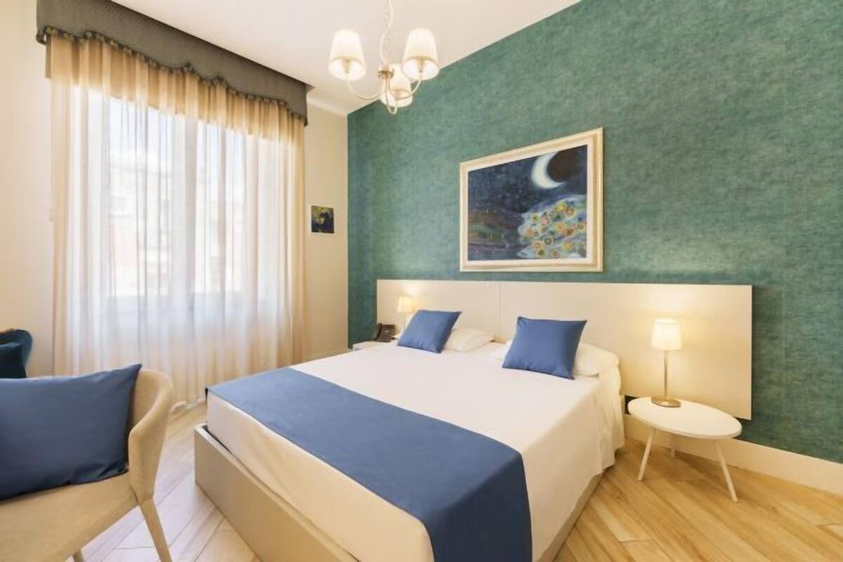 Ein Hotelzimmer mit Bett, zwei Nachttischen, einem Sessel, einem Schminktisch, einem Bild und einem Fenster mit Vorhängen.