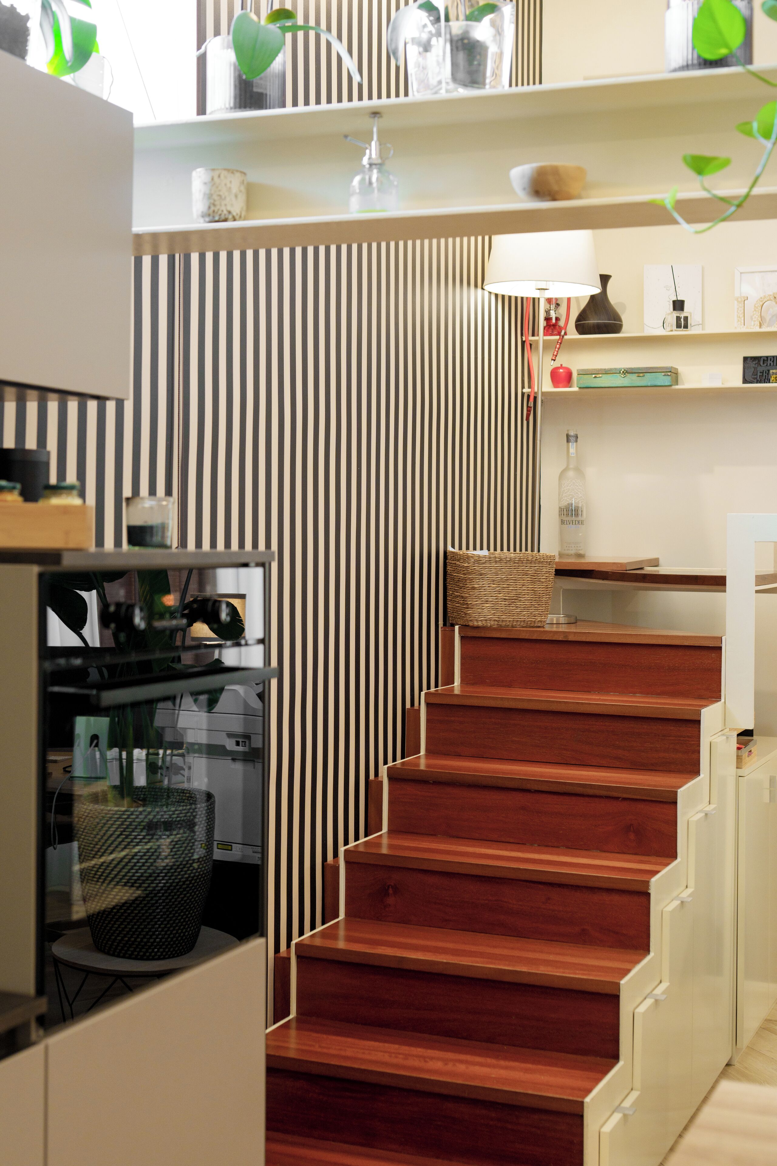 Een moderne keuken met een houten trap, een gestreepte wand en diverse keukengadgets.