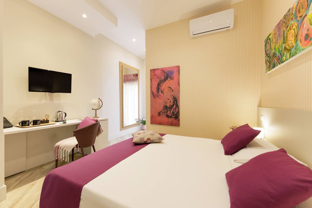 Ein Hotelzimmer mit Bett, Schreibtisch, Stuhl, Fernseher und Klimaanlage.