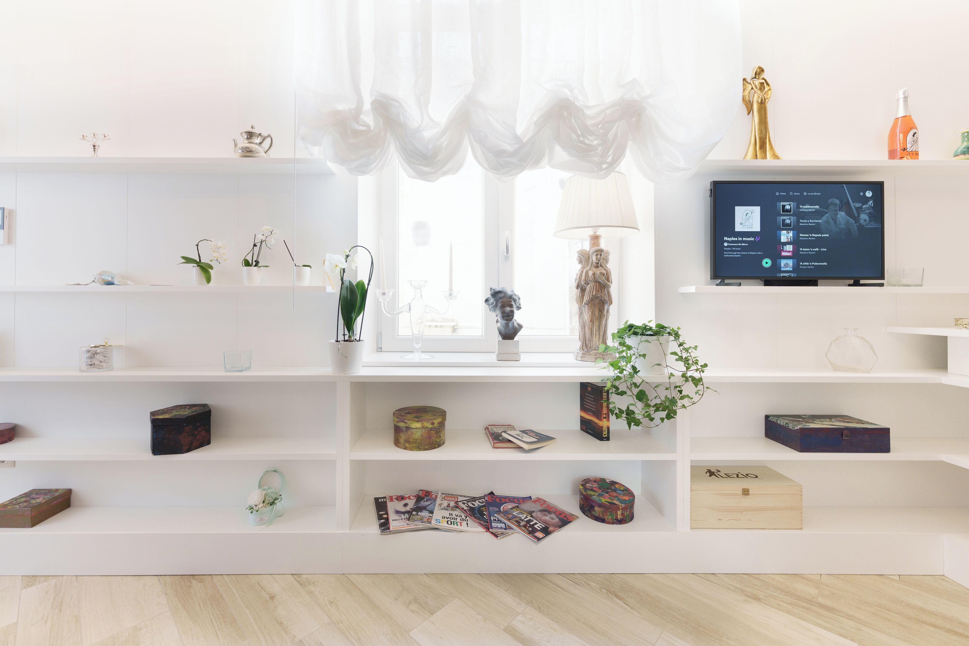 Una sala de estar moderna con estanterías blancas, un televisor y varios objetos decorativos.