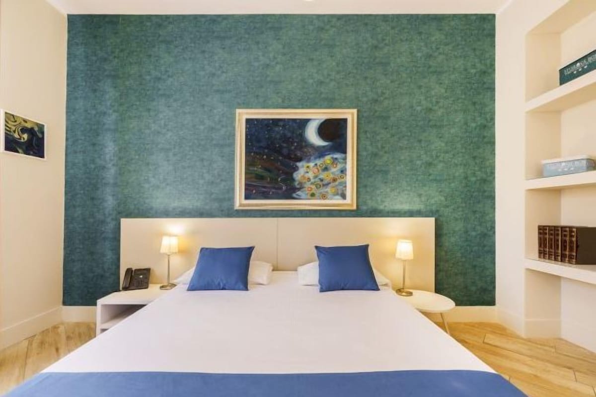 A hotel room with a large bed, two bedside tables with lamps, a green textured wall, and a framed picture of a night sky.
