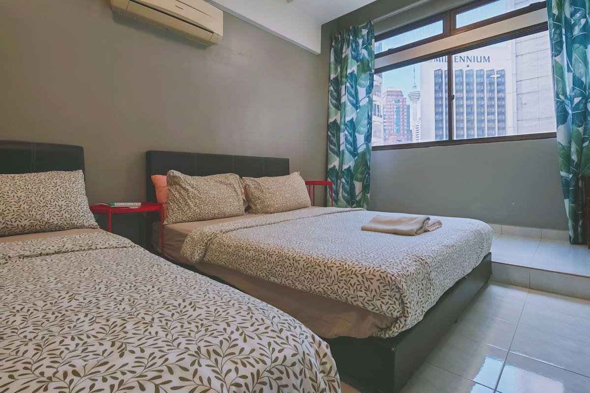 A hotel room with two beds, a window with a view of a building, and an air conditioning unit.