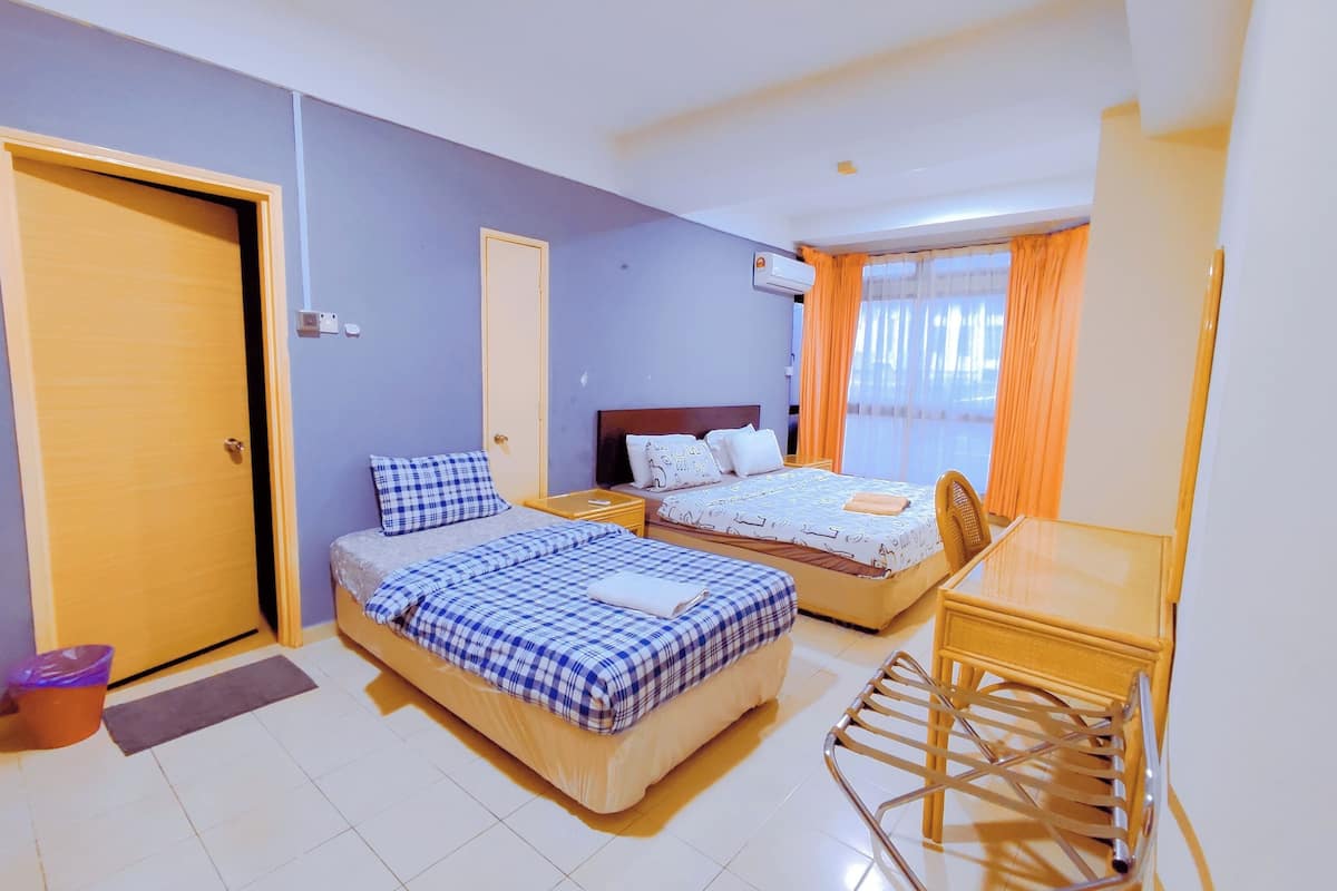 A hotel room with two beds, a desk, a chair, a small table, a waste bin, and a door.