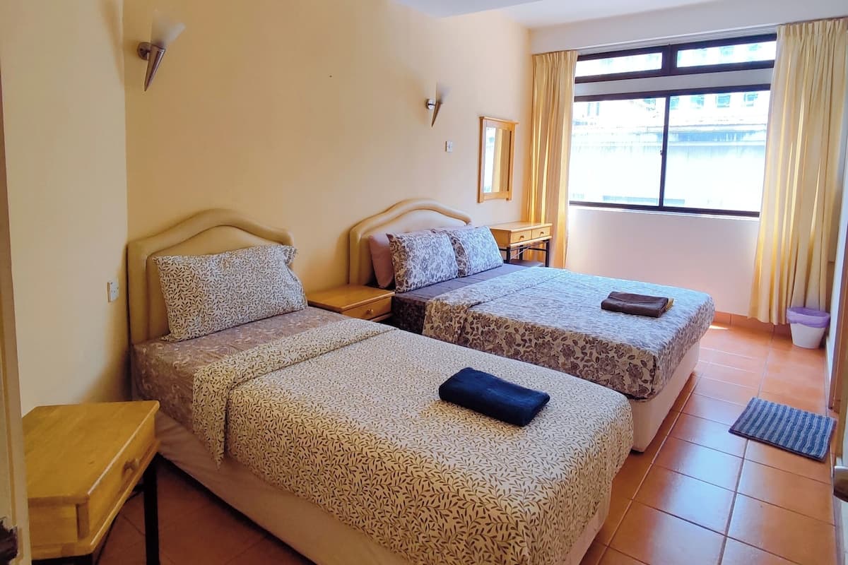 A hotel room with two beds, a ceiling fan, a window with curtains, and a small table.