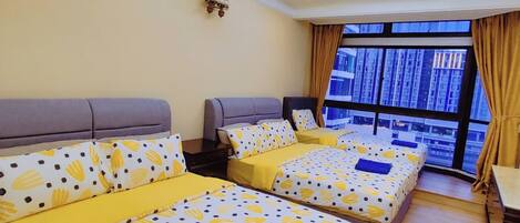 A hotel room with three beds, a ceiling fan, and a large window with a view of buildings.