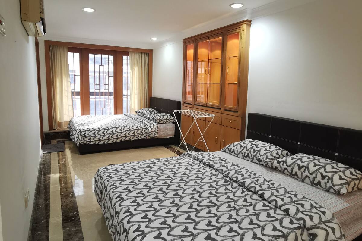 A hotel room with two beds, a wardrobe, a radiator, and a window with curtains.