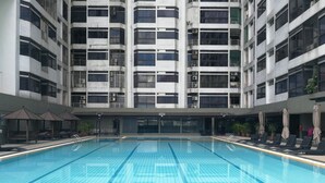 A swimming pool with tiled lanes, surrounded by a building with multiple balconies and a covered area with lounge chairs and umbrellas. - Pavilion Fahrenheit 88 - AJ home (Kuala Lumpur)