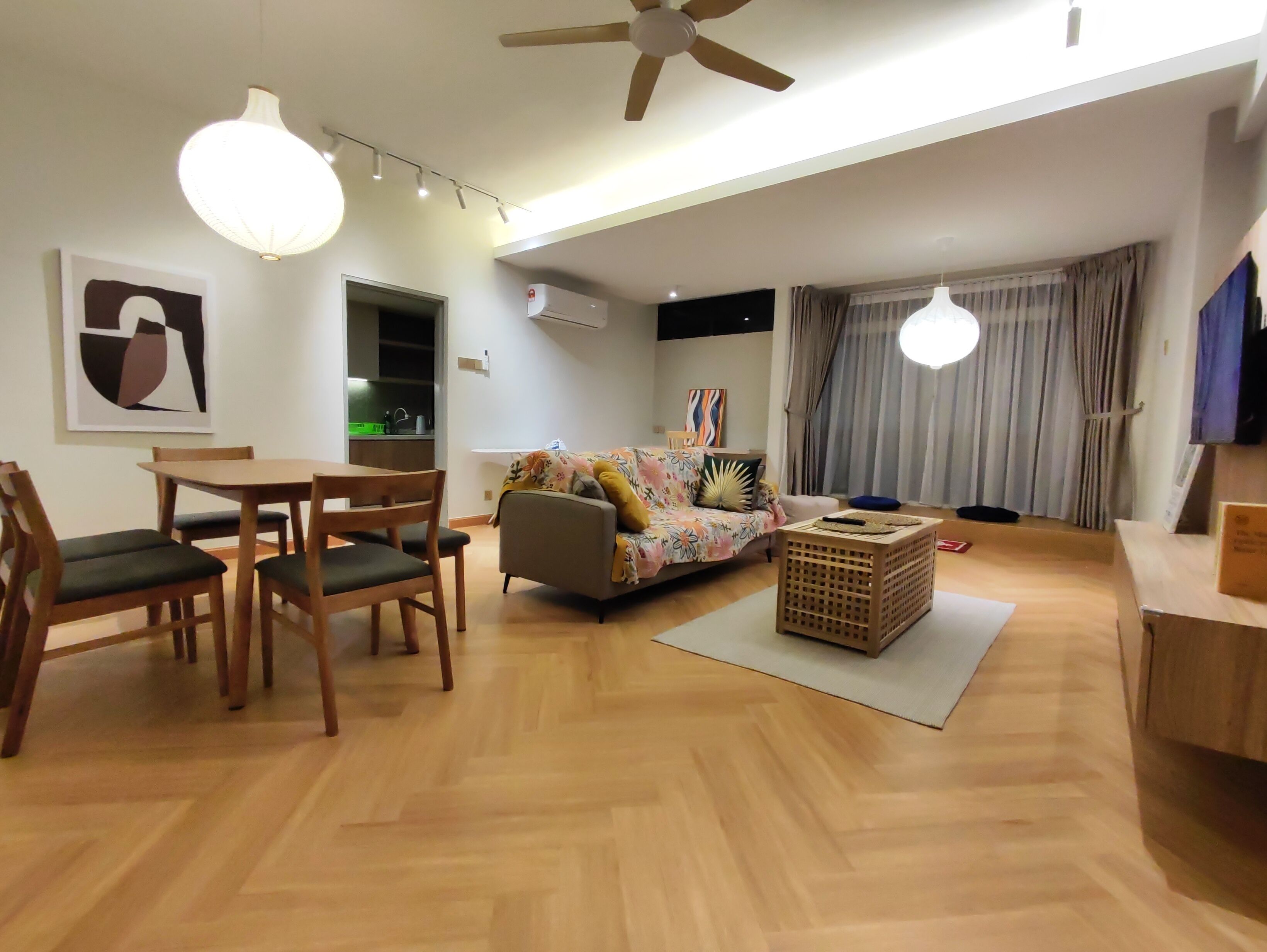 Una sala moderna con piso de madera, un sofá, una mesa de comedor con sillas, un ventilador de techo y un equipo de aire acondicionado.