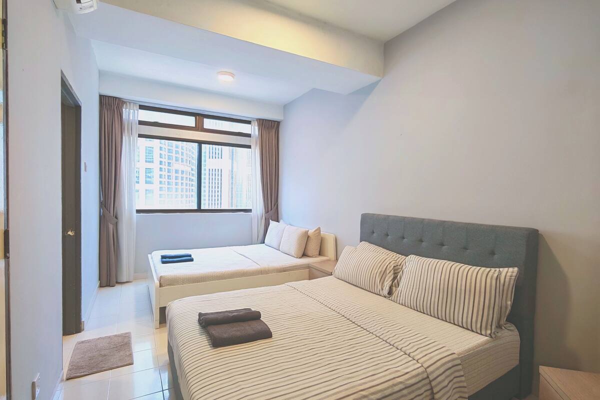 A hotel room with a large bed, a smaller bed, a window with curtains, a ceiling light, and a tiled floor.