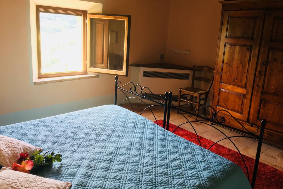 A bedroom with a bed, a window, a wooden wardrobe, and a radiator.