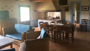 Een gezellige woonkamer met een bank, eettafel en stoelen. Achtergrond is een keuken met een spoelbak en aanrecht.