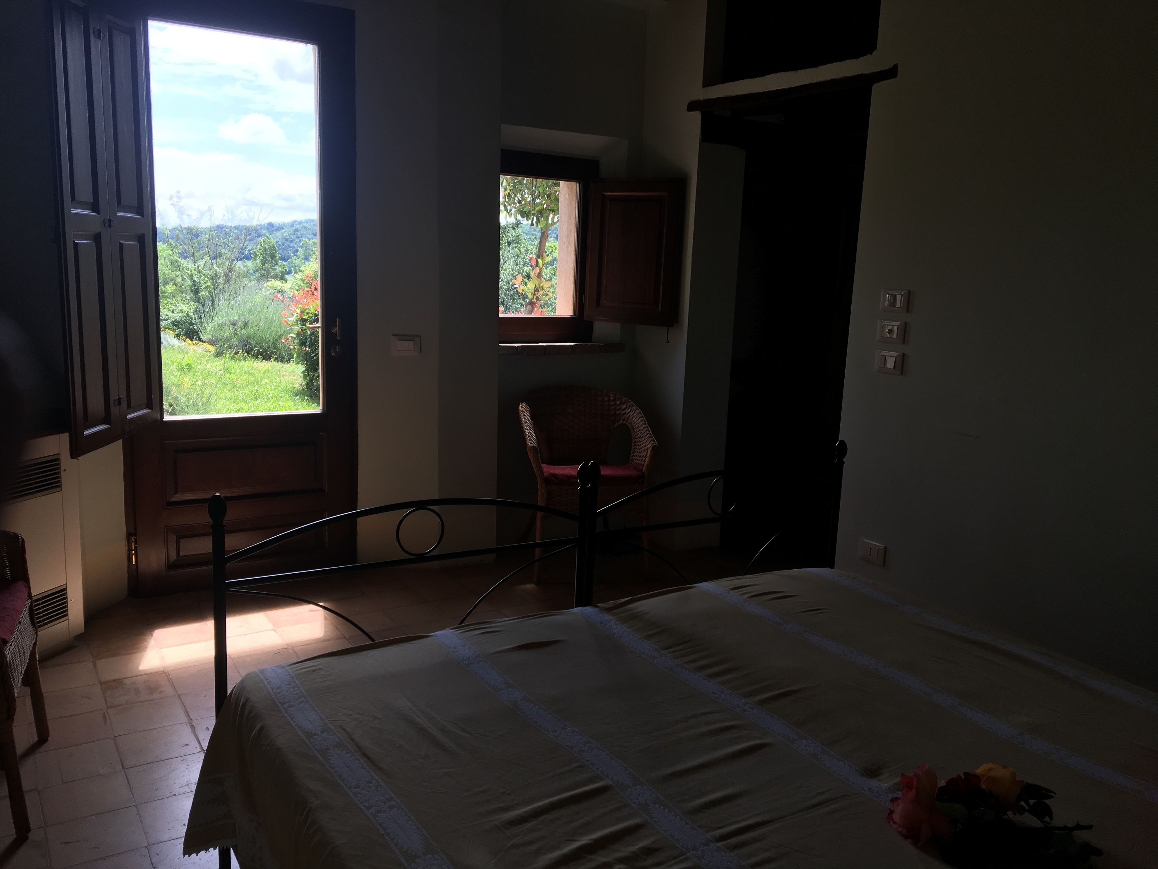 Ein Schlafzimmer mit einem Bett, einem Sessel, einem Fenster mit Blick auf Grünflächen und einer Tür.