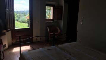 Ein Schlafzimmer mit einem Bett, einem Sessel, einem Fenster mit Blick auf Grünflächen und einer Tür.