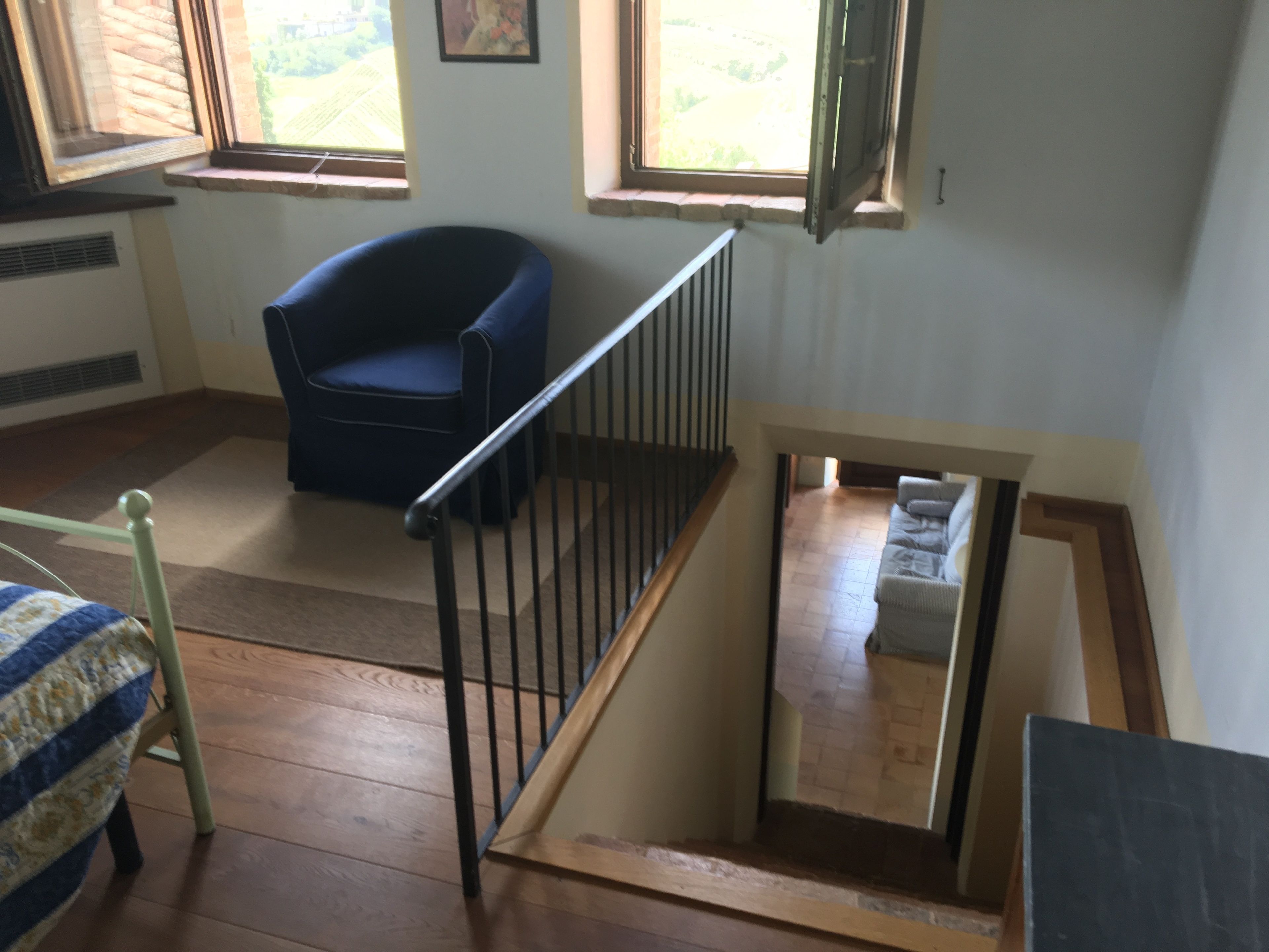 Una stanza con una sedia blu, una scala in legno e una finestra che si affaccia sul verde.
