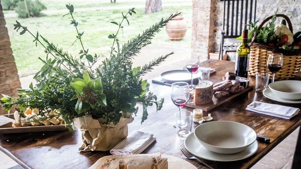 A rustic outdoor dining table set with bread, cheese, and wine glasses, surrounded by greenery and a stone wall. - Bio Tenuta di Paganico - I Roggeti (Civitella Paganico)