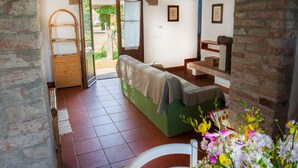 A room with a bed, a wooden bench, a table with a vase of flowers, and a view through an open door. - Bio Tenuta di Paganico - I Roggeti (Civitella Paganico)