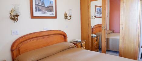 A bedroom with a wooden bed, bedside tables, a nightstand, a wardrobe, and a framed picture on the wall.