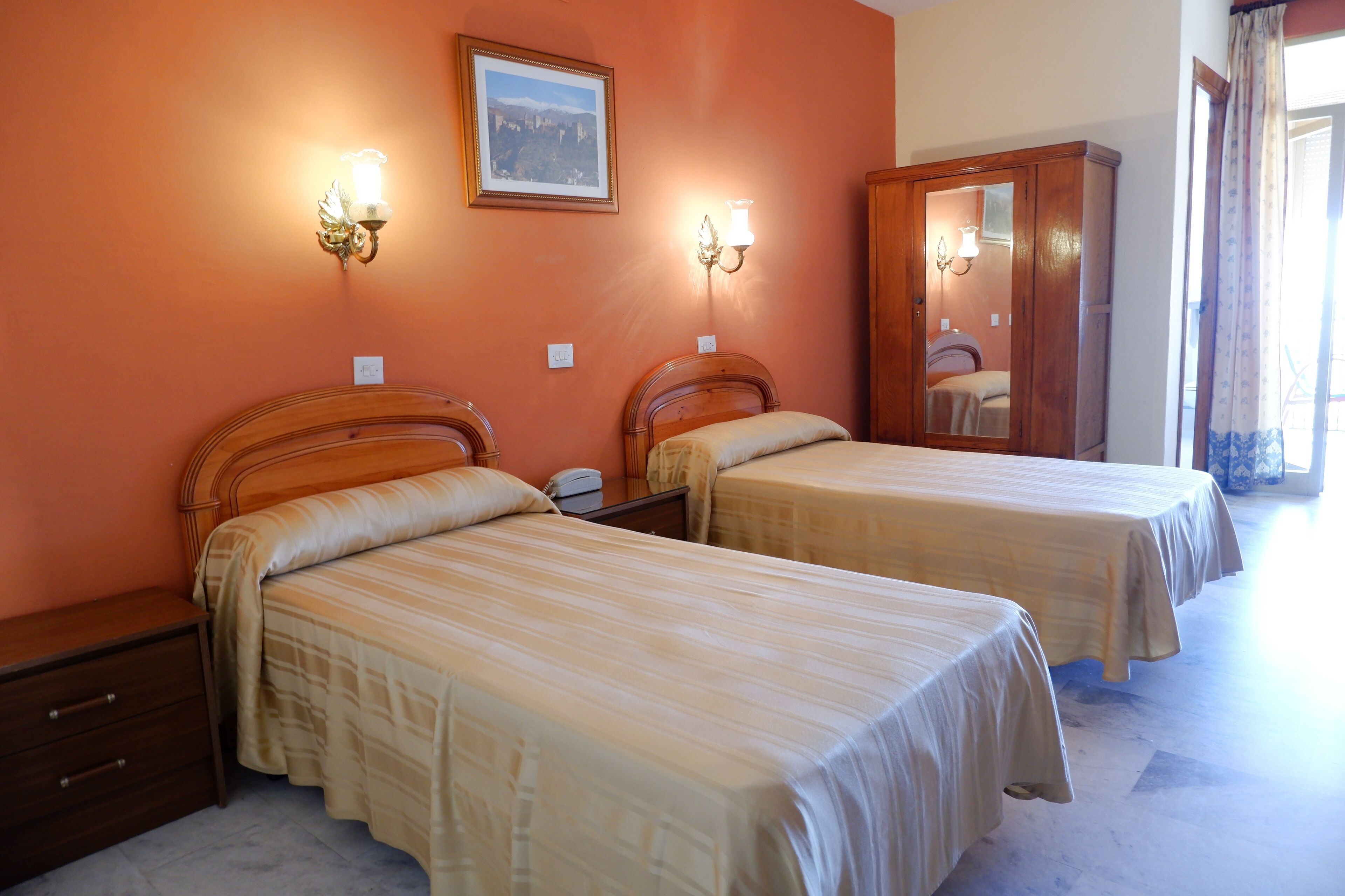 Habitación de hotel con dos camas, un armario de madera y lámparas fijadas a la pared.
