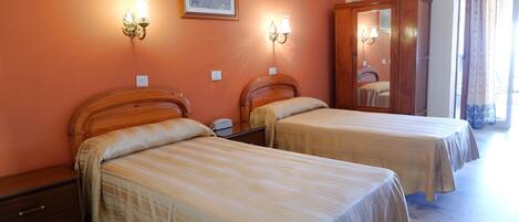 Habitación de hotel con dos camas, un armario de madera y lámparas fijadas a la pared.