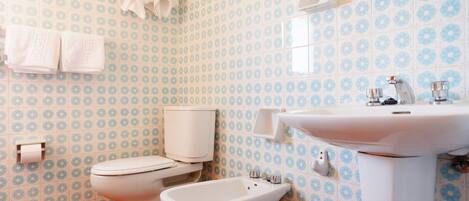 A bathroom with a toilet, bidet, and sink, all in white.