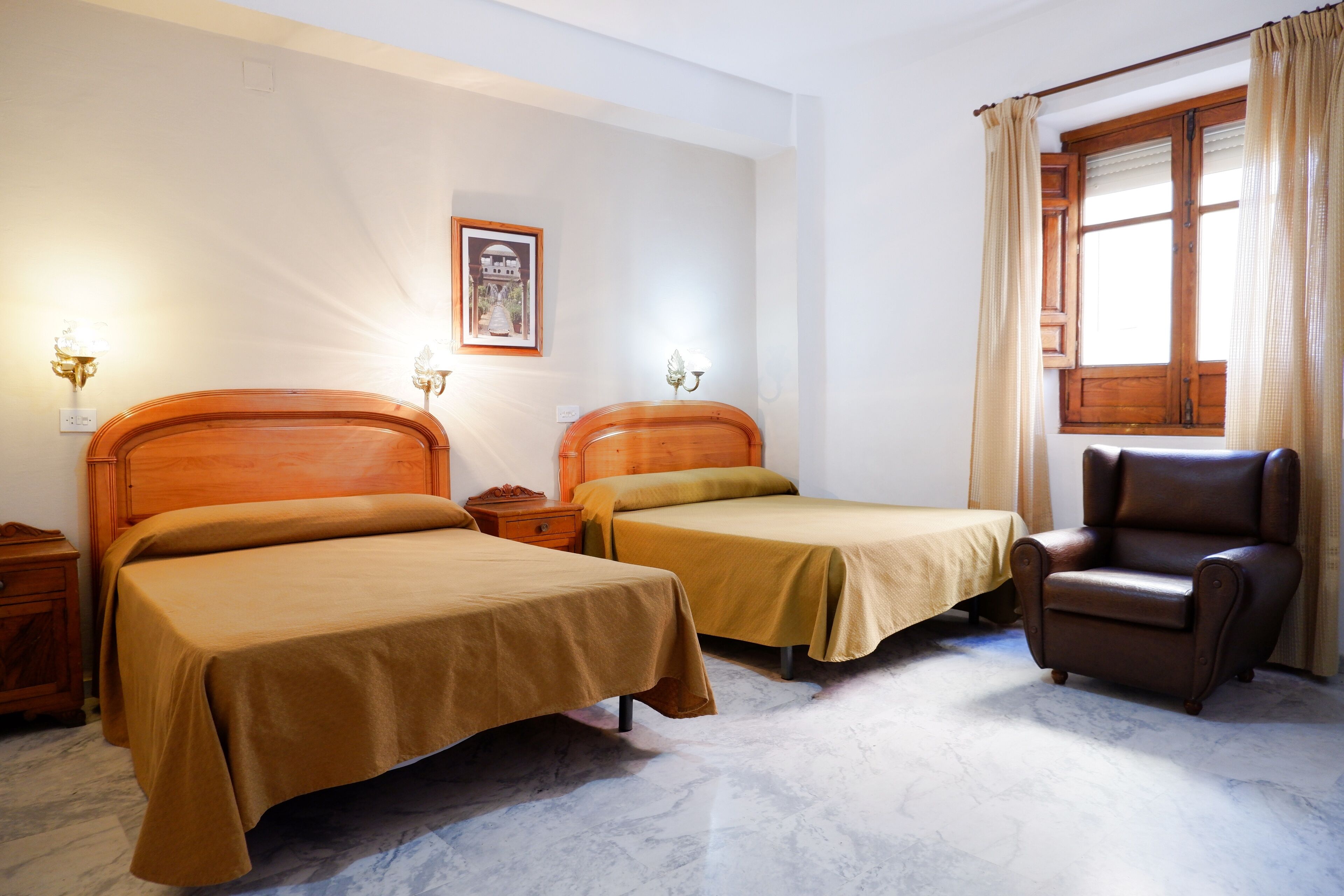 Una habitación de hotel con dos camas individuales, una silla de madera y un ventanal con cortinas.