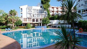 Une piscine avec des chaises longues et un bâtiment doté de balcons en arrière-plan.