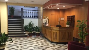 Un hall d’hôtel avec un sol à carreaux, un comptoir d’accueil et des plantes en pot.