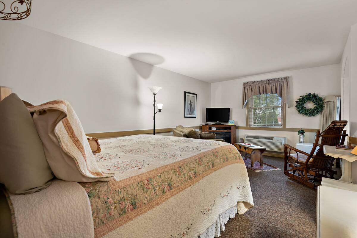 A bedroom with a large bed, a desk, a chair, a television, and a window with curtains.