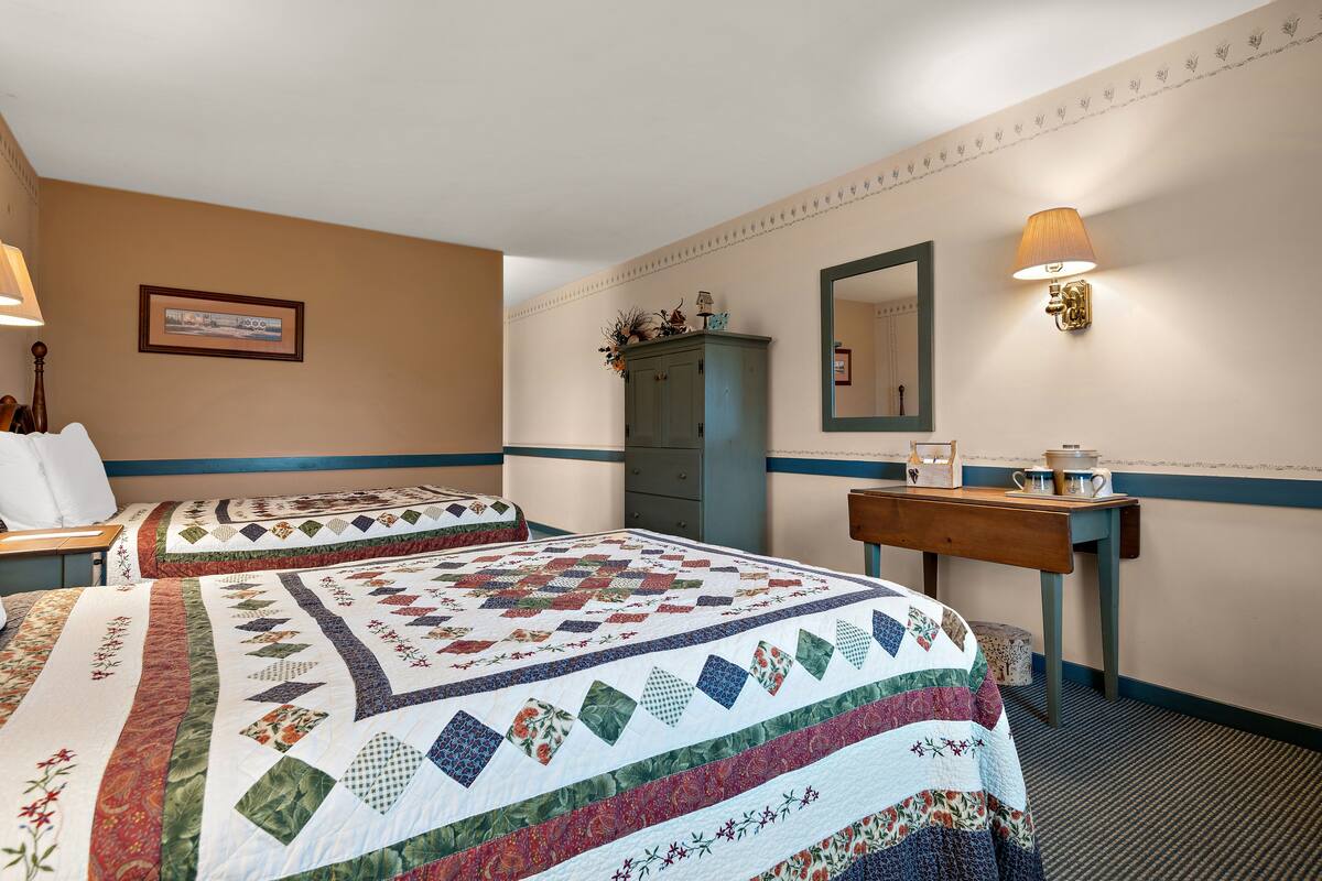 A hotel room with two beds, a dresser, a mirror, and a lamp.