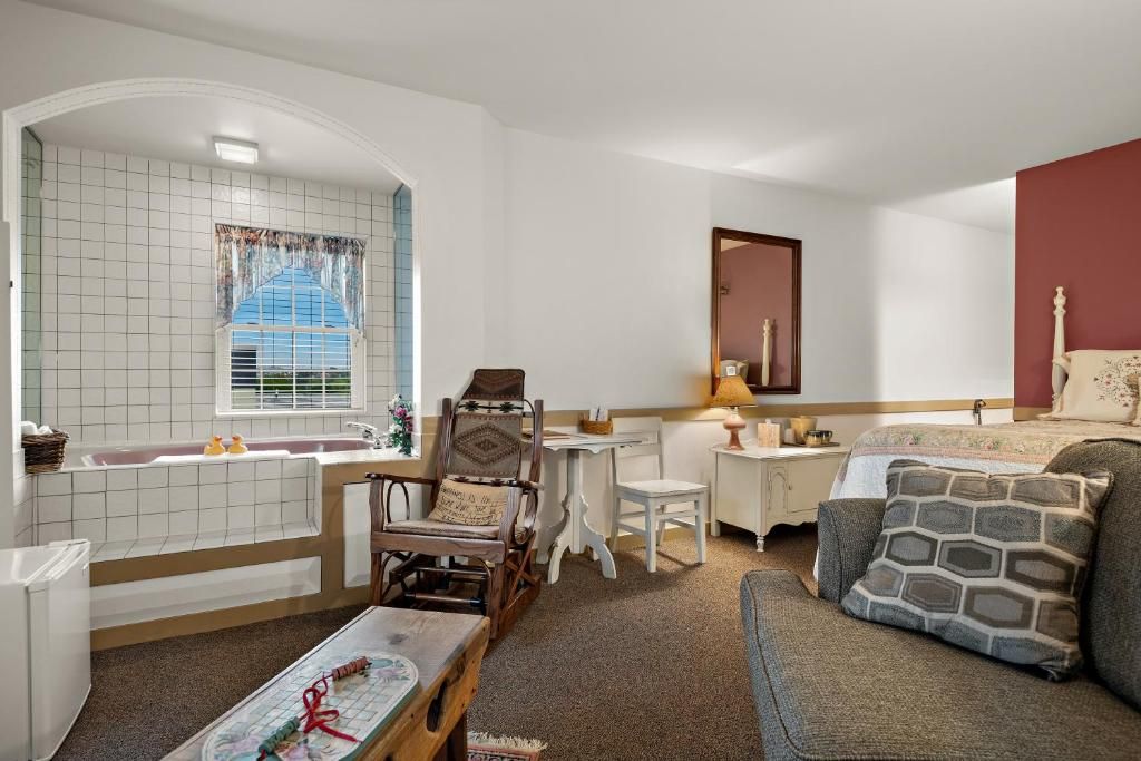 A room with a bathtub, a desk, a chair, a sofa, and a window with curtains.
